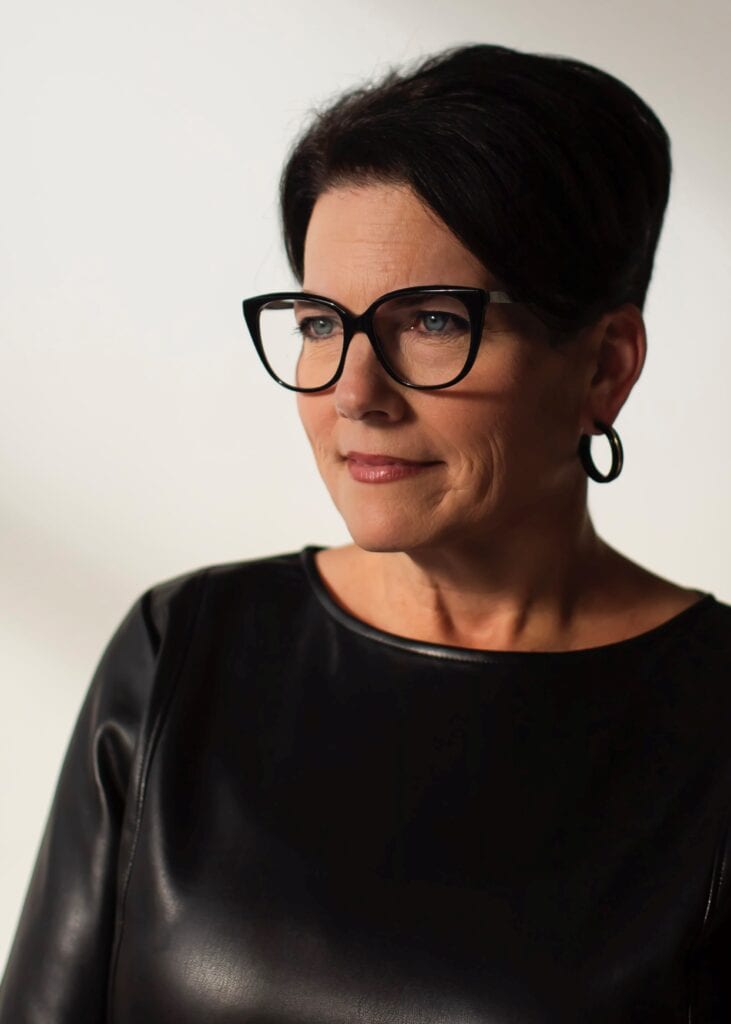 A photo of a woman with short, dark hair and glasses smiling to the side