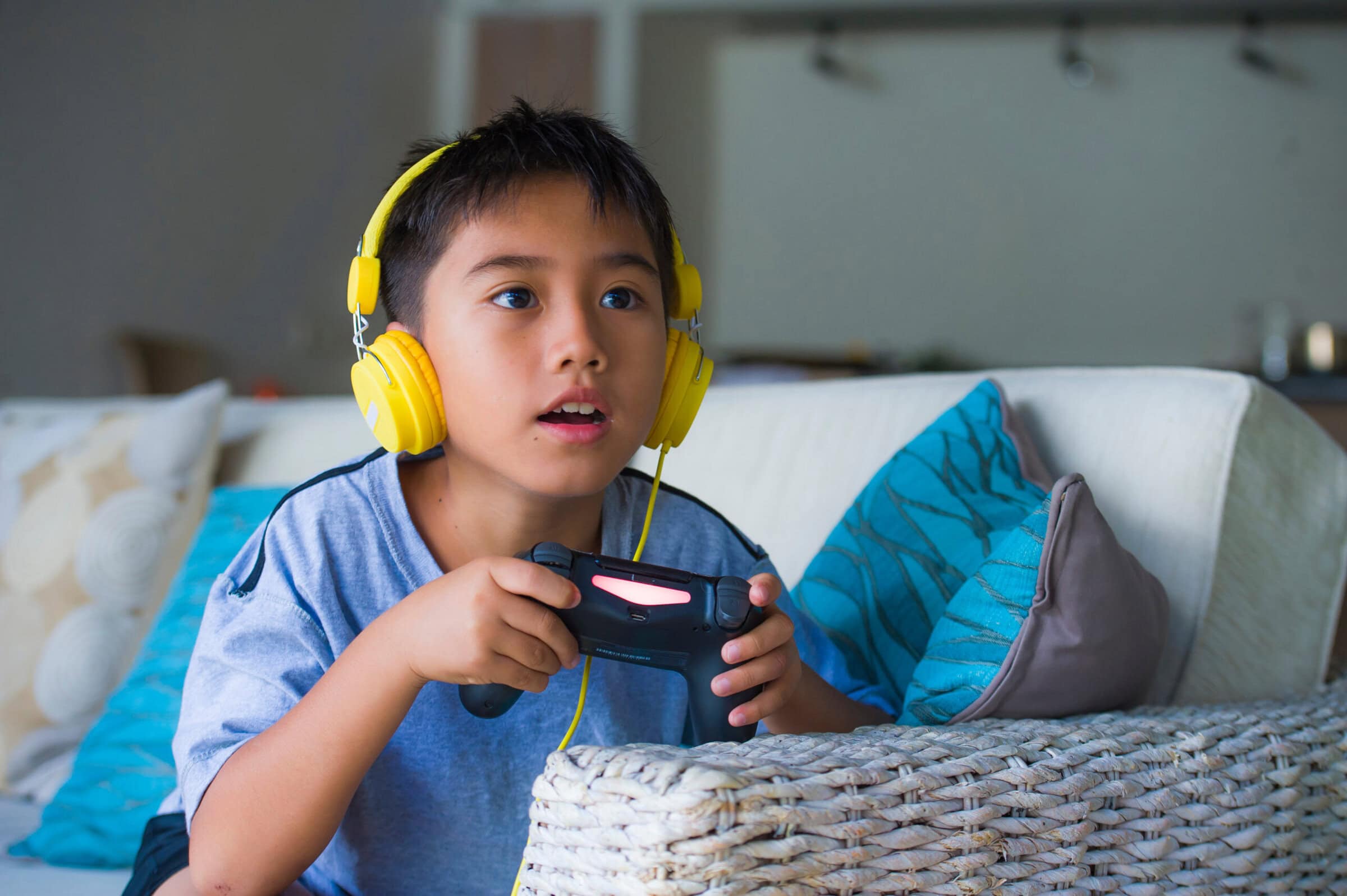 young latin little child excited and happy playing video game online with headphones holding controller having fun sitting on couch in kid gaming addiction