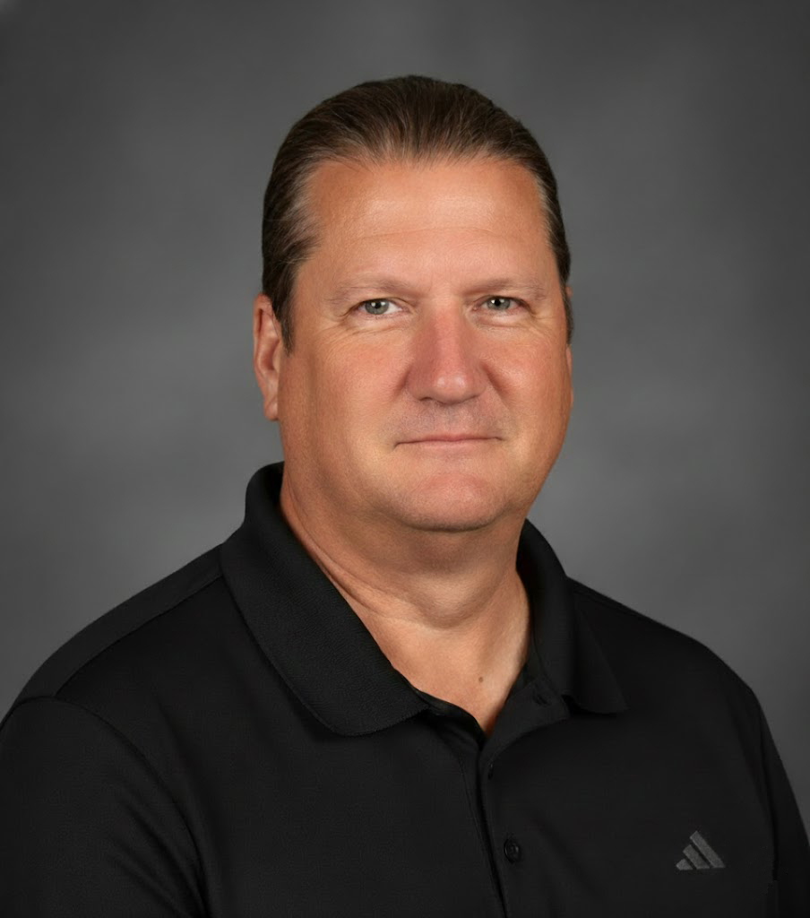 A man with a pleasant disposition is smiling, wearing a dark black polo shirt.