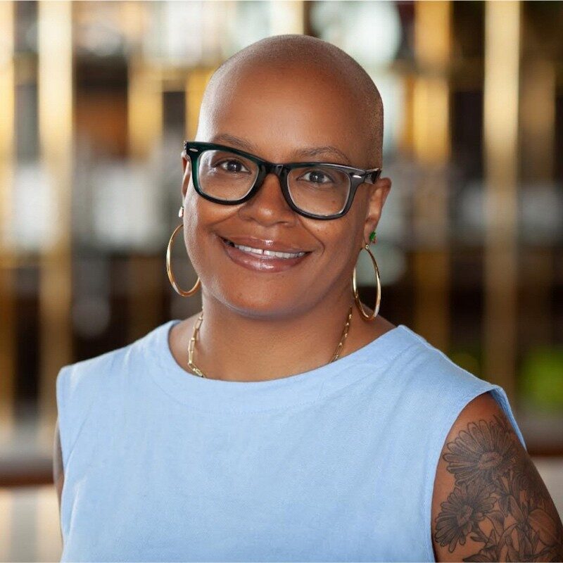 Empowered woman with glasses and tattoos smiling at CoSN conference.
