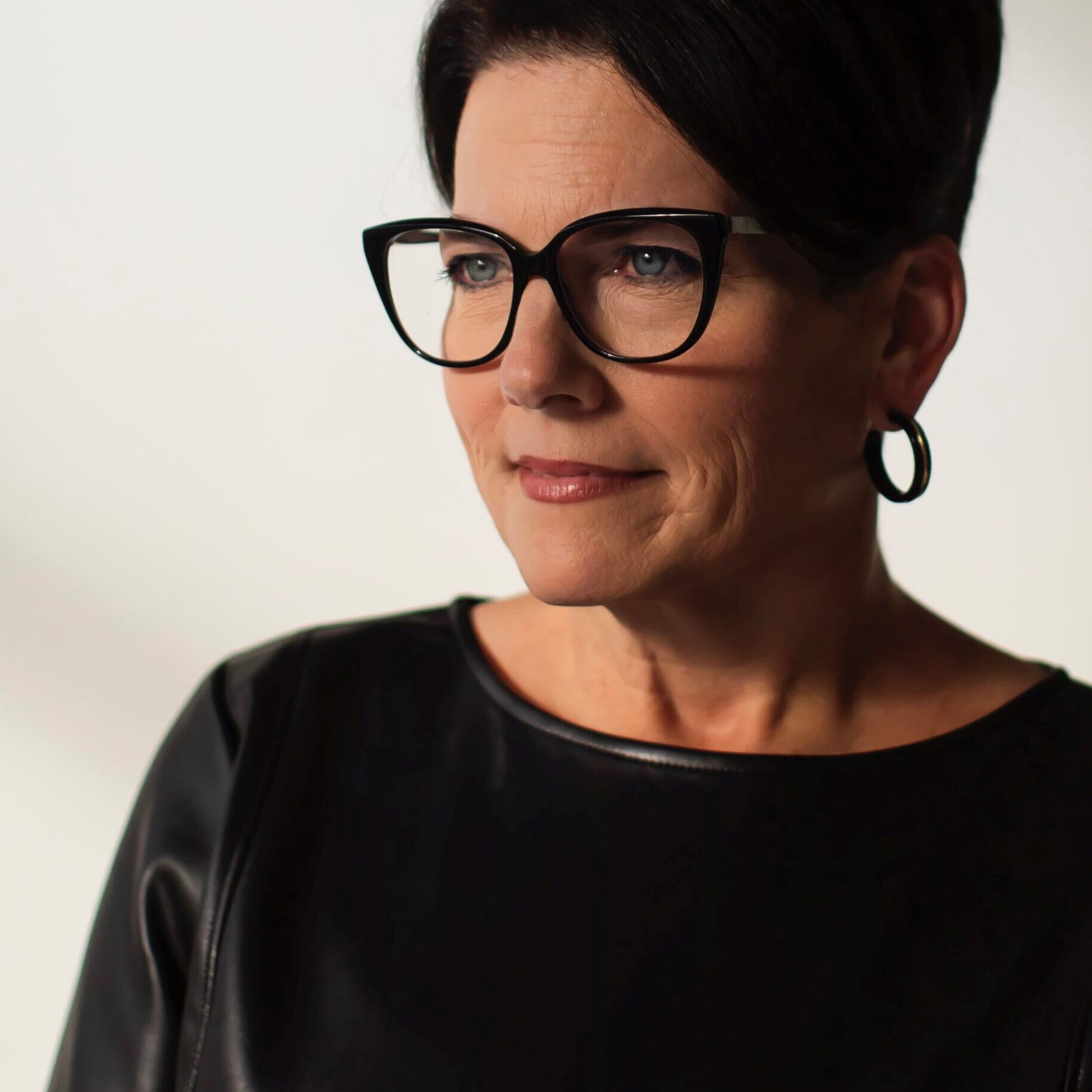 A photo of a woman with short, dark hair and glasses smiling to the side