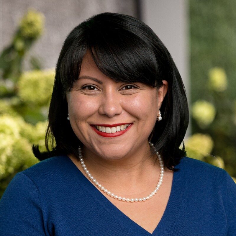Professional woman smiling at outdoor event, emphasizing education and leadership.